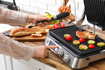 Woman cooking tasty steaks and vegetables on modern electric grill in kitchen
