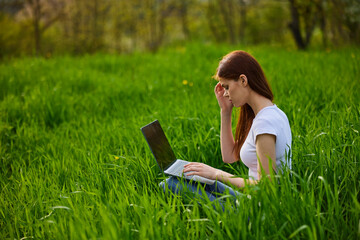 a woman works remotely at a laptop being outdoors in tall grass