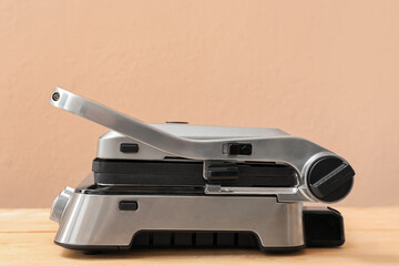 Modern electric grill with closed lid on wooden table against beige background