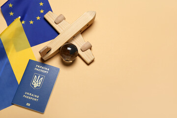 Passport, wooden airplane with flags of Ukraine and European Union on beige background