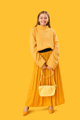 Fashionable young woman in knitted sweater and skirt on yellow background