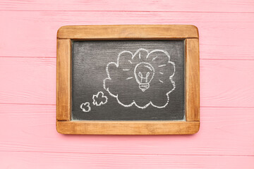 Chalkboard with drawn speech bubble and light bulb on pink wooden background. Insight concept