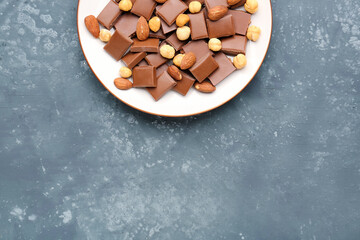Plate with pieces of tasty chocolate and nuts on blue background