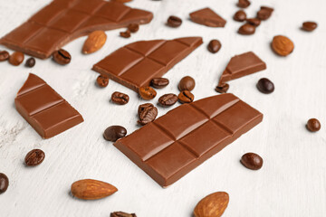 Pieces of tasty chocolate, almonds and coffee beans on light wooden background, closeup