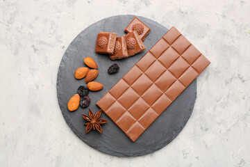 Slate board with tasty chocolate, almonds, raisins and anise on light background