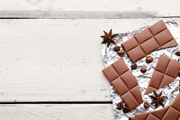 Foil with tasty chocolate, coffee beans and anise stars on light wooden background