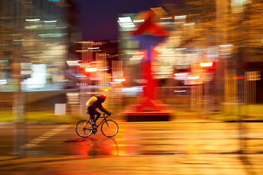 Cyclist on wet road. Person on the slick way to work in the rain in the city at night. Panning shot. Germany, Stuttgart.