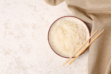 Bowl with tasty rice noodles and chopsticks on white grunge table