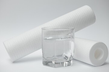 Water filters. Carbon cartridges and a glass on a yellow background. Household filtration system