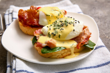 Plate with tasty eggs Benedict on grey grunge table, closeup