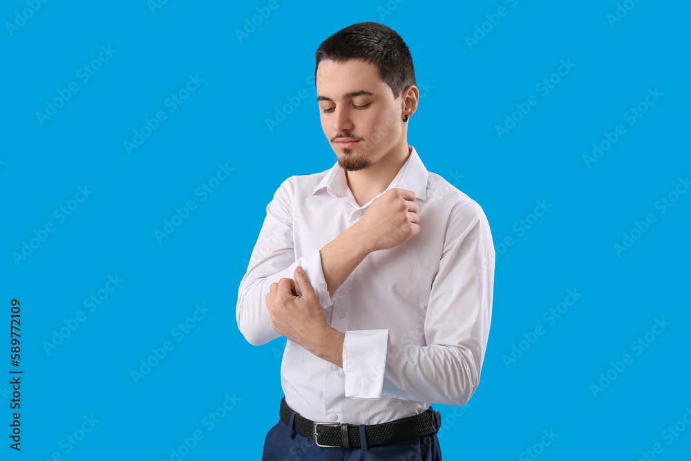 Poster Young businessman rolling up his sleeve on light blue background