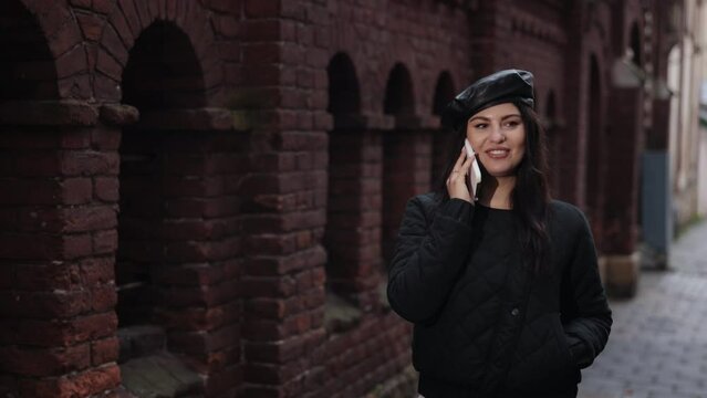 talking pedestrian, lady talking, city walker. Young woman converses on phone as she makes her way down pavement.