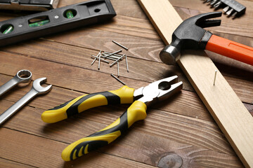 Pliers, nails, plank and hammer on wooden table