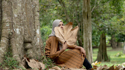 Muslim woman sitting and covering her face with dried leave in the forest.