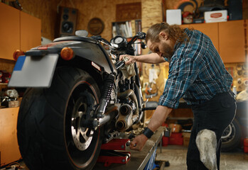 Fototapeta na wymiar Motorbike mechanic working with screwdriver repairing motorcycle in garage