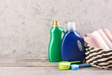 Laundry detergents and basket with towels on wooden table against grey background
