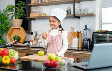 Millennial Asian young little cute girl chef daughter with white tall cook hat and apron standing...