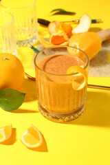 Glass of healthy orange smoothie and ingredients on yellow background