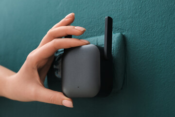 Woman plugging black WiFi repeater in electric socket on green wall
