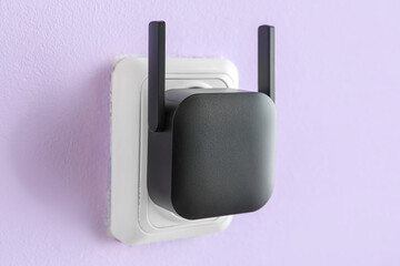 Black WiFi repeater in electric socket on lilac wall