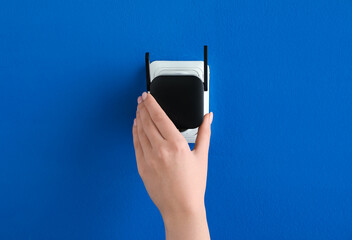 Woman plugging black WiFi repeater in electric socket on blue wall