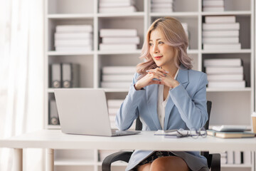 Asian Businesswoman Using laptop computer and working at office with calculator document on desk, doing planning analyzing the financial report, business plan investment, finance analysis concept.
