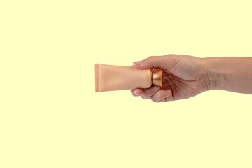 Female hand holds cosmetic product in tube, bottle, lotion or serum on yellow background.