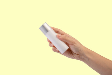 Female hand holds cosmetic product in tube, bottle, lotion or serum on yellow background.