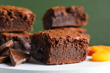 Board with pieces of tasty chocolate brownie on green background, closeup