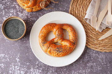 Plate with tasty pretzel and poppy seeds on grunge background