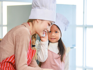 Asian young female chef housewife mother and little cute girl daughter wears white tall cook hat and apron smiling posing looking  at home kitchen.