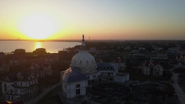 Statue atop abandoned dome building, sunset aerial orbits golden lake