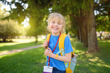 Elementary student boy with backpack, bottle of water and name badge on his neck goes to school....