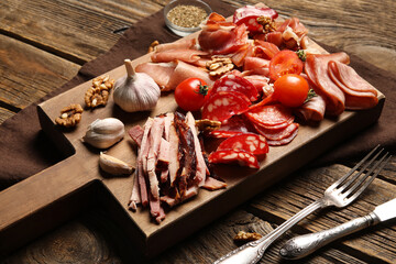 Board with assortment of tasty deli meats on wooden background