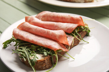 Tasty ham bruschetta with arugula on green wooden background