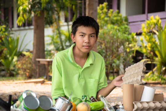 Young asian boy sorting broken eggshells and other garbages and putting them into the boxes infront of him in the park, nature care and environment love concept.