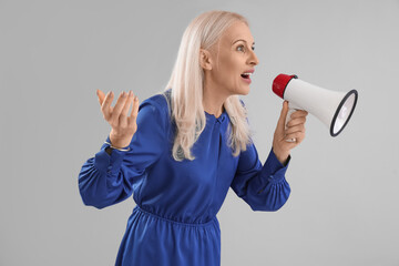 Mature woman shouting into megaphone on grey background