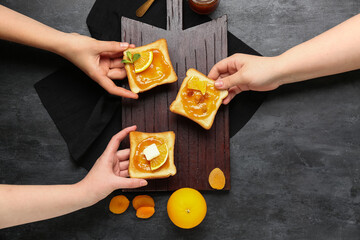 Women holding tasty toasts with orange jam on dark background