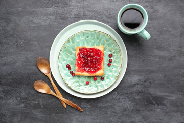 Tasty toast with cranberry jam and cup of coffee on dark background