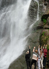 A young men and women is facing the waterfall with her hands up. No faces.  back, rear view. traveling team.