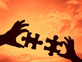 black Silhouette of two hand holding couple of jigsaw puzzle piece on blue sky with clouds...