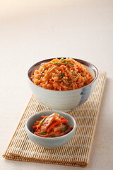 Fototapeta na wymiar Kimchi stir fried rice, korean food in ceramic bowl and a small bowl of kimchi on bamboo place mat on white linen cloth background.