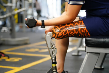 Young female with one prosthetic leg warms up by lifting light weights. Concept of living a woman's...