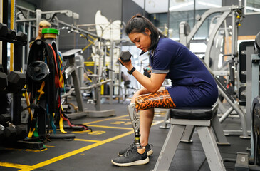 Young female with one prosthetic leg warms up by lifting light weights. Concept of living a woman's life with a prosthetic limb.