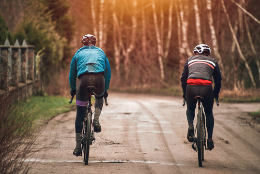 Two bike riders from the back. Modern gravel bicycle. Riding a bike in rainy weather. Cyclist from behind wearing a safety helmet.