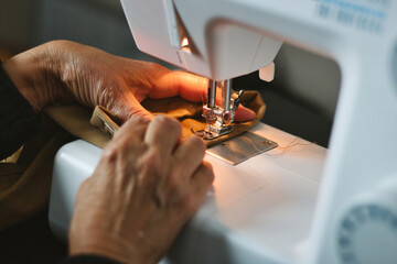 Close-up shot of an older woman's hands using a domestic sewing machine to sew thread onto material