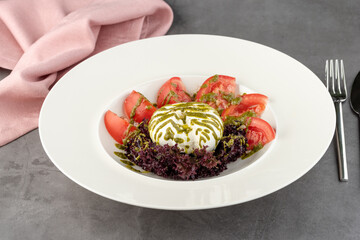 Burrata cheese with tomatoes and fresh greens on a white porcelain plate