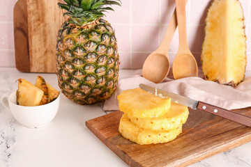 Wooden board with cut pineapple on table in kitchen