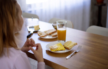 A little blonde girl is having breakfast in the kitchen with an omelette, a sandwich with butter and cheese and orange juice. Delicious and healthy breakfast of natural products for schoolchildren.