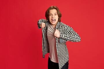 Portrait of young man screaming and ripping off clothes on body over red background. Wide range of emotions